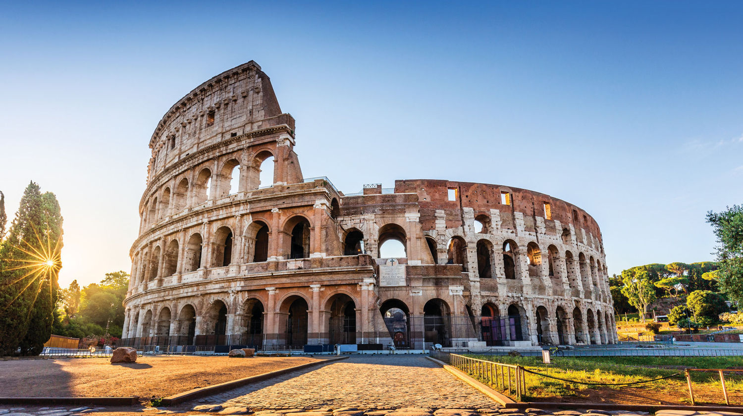 Vista do Coliseu em Roma sob um céu azul, com a estrutura histórica iluminada pela luz do sol
