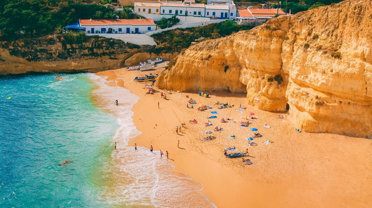 Aerial view of Praia da Marinha in Lagoa, Algarve, with golden cliffs, turquoise water, and sunbathers on the sandy beach.