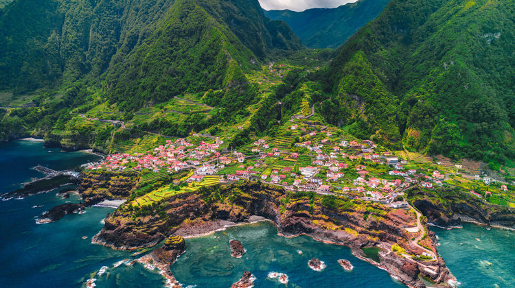 Aerial view of Seixal on Madeira’s north coast, with the village and waterfront set between steep green mountains and the Atlantic Ocean.