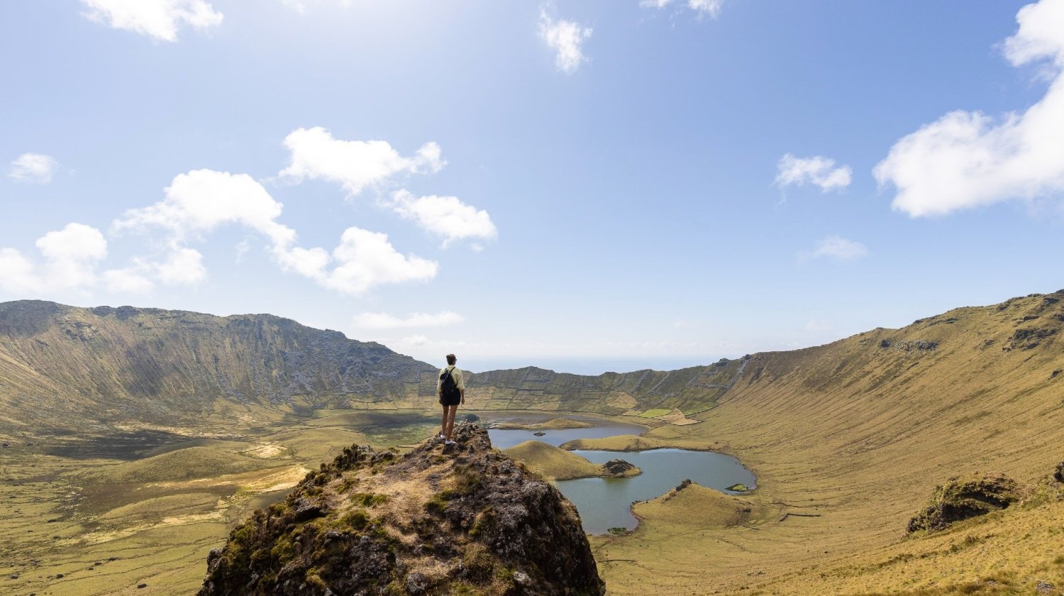 Panoramic view of the Caldeirão volcanic crater with a person stading beside the lagoons and rugged terrain  on Corvo Island, Azores.