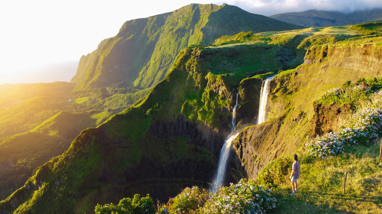 Scenic view of a tall waterfall cascading down lush cliffs at Fajã Grande, Flores Island, during golden hour.