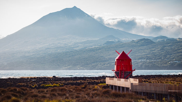Red lighthouse in Lajes do Pico with Mount Pico in the background and the ocean in the foreground, on Pico Island.