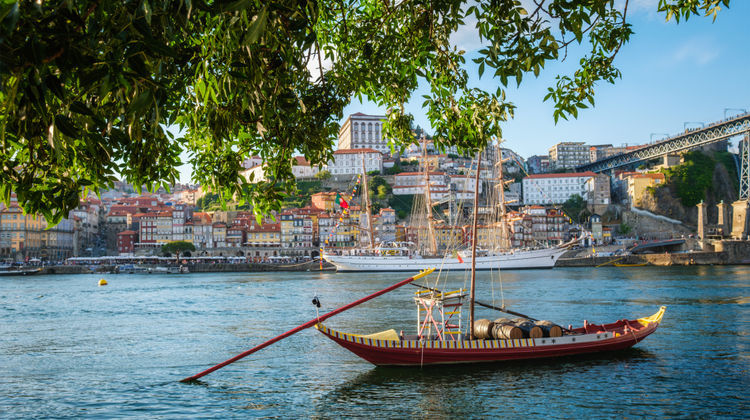 Wooden Rabelo boats floating on the Douro River with Porto’s colorful old town and riverside buildings in view.