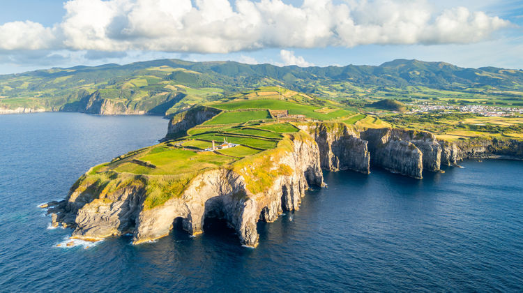 Aerial view of the rugged volcanic coastline at Ponta do Cintrão, showing natural stone arches and steep cliffs meeting the deep blue Atlantic Ocean
