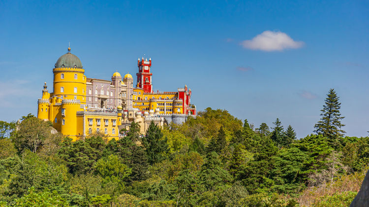 Colorful Pena Palace in Sintra, Portugal, with yellow and red towers rising above the forest.