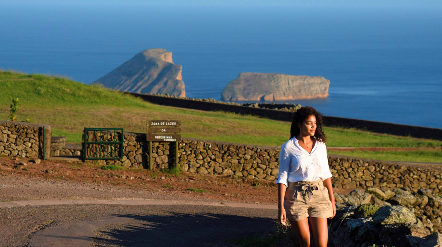 Woman enjoying the scenic cliffs of Terceira Island, Azores, with Ilhéus das Cabras in the background.