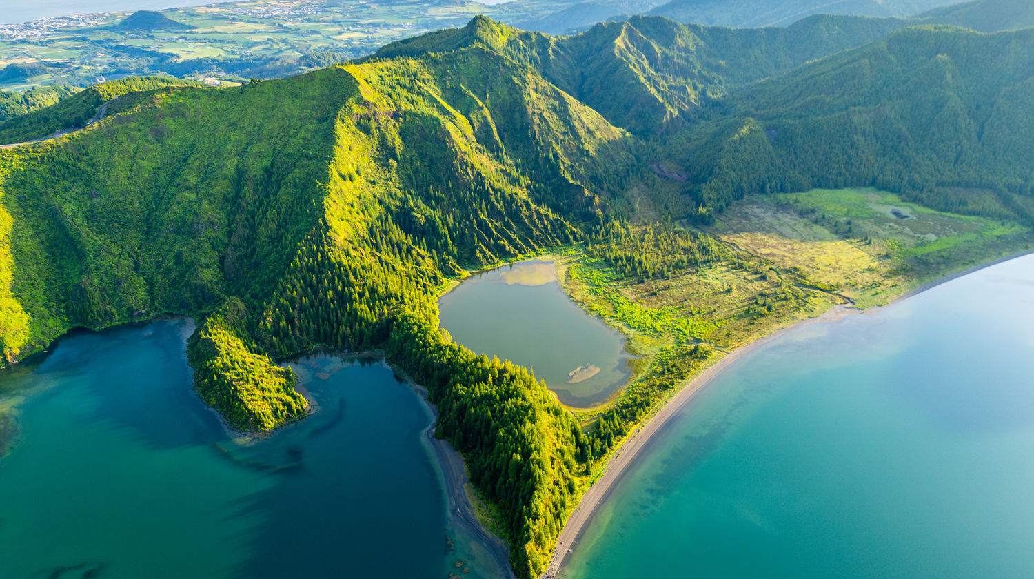 Aerial view of the edge of Lagoa do Fogo and the surrounding trail path winding through vibrant green nature on São Miguel, Azores