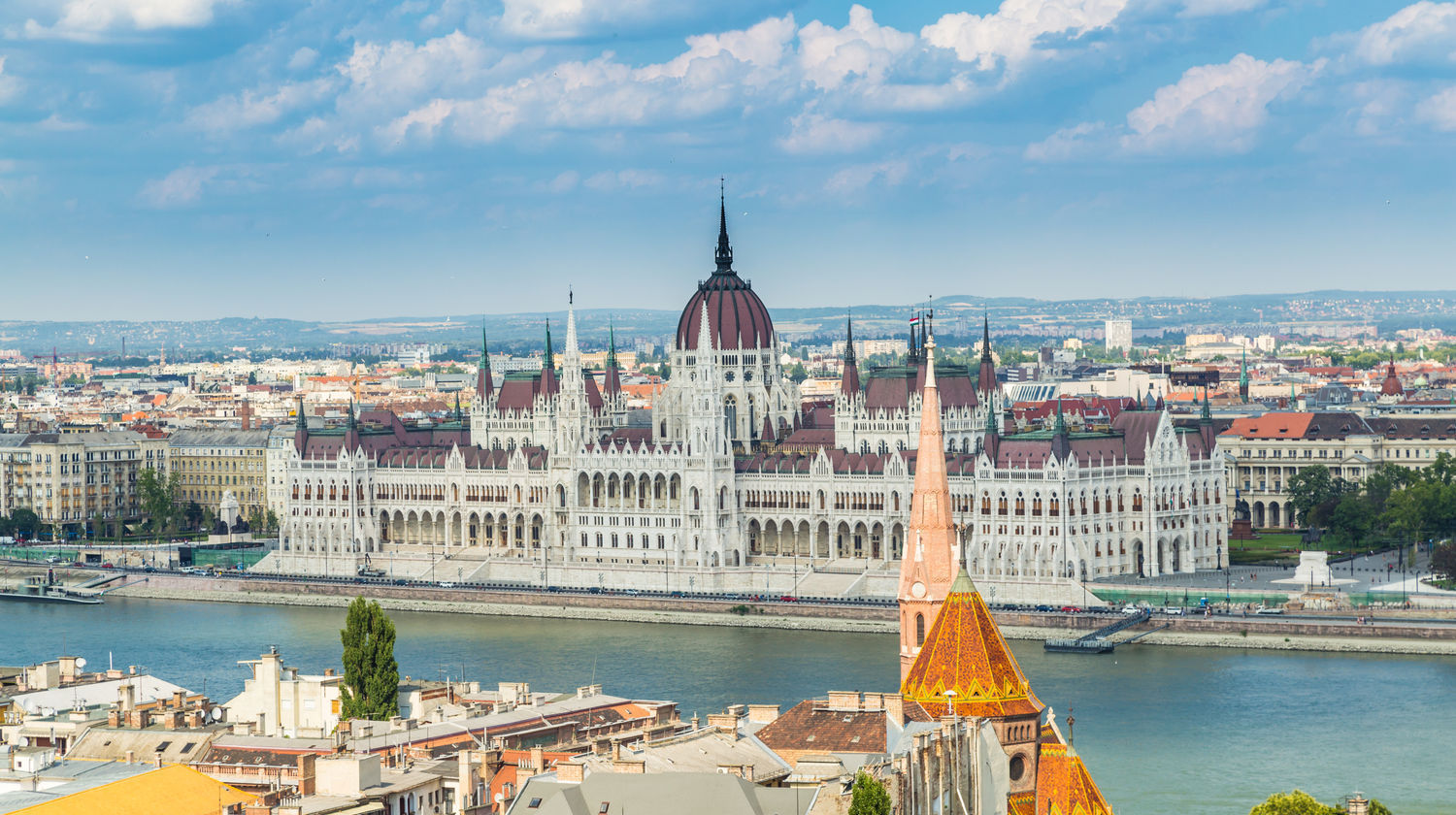 The Hungarian Parliament Building rises along the Danube River in Budapest, Hungary, featuring a large central dome, detailed spires, and a riverside promenade.