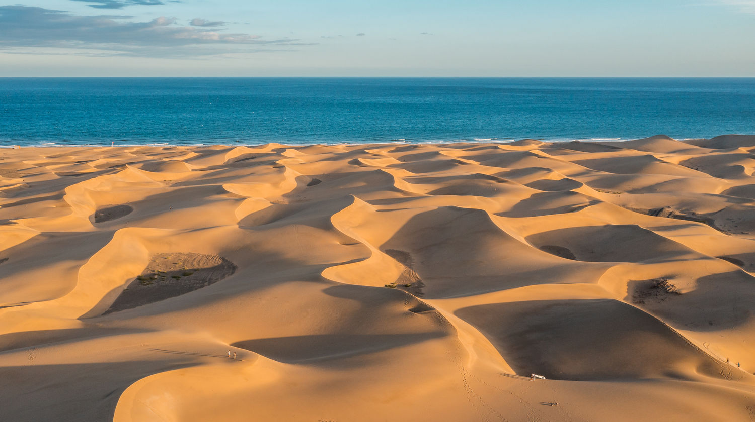 Maspalomas dunes in Gran Canaria, Canary Islands, Spain, with rolling golden sand formations and a person walking across the desert-like landscape.
