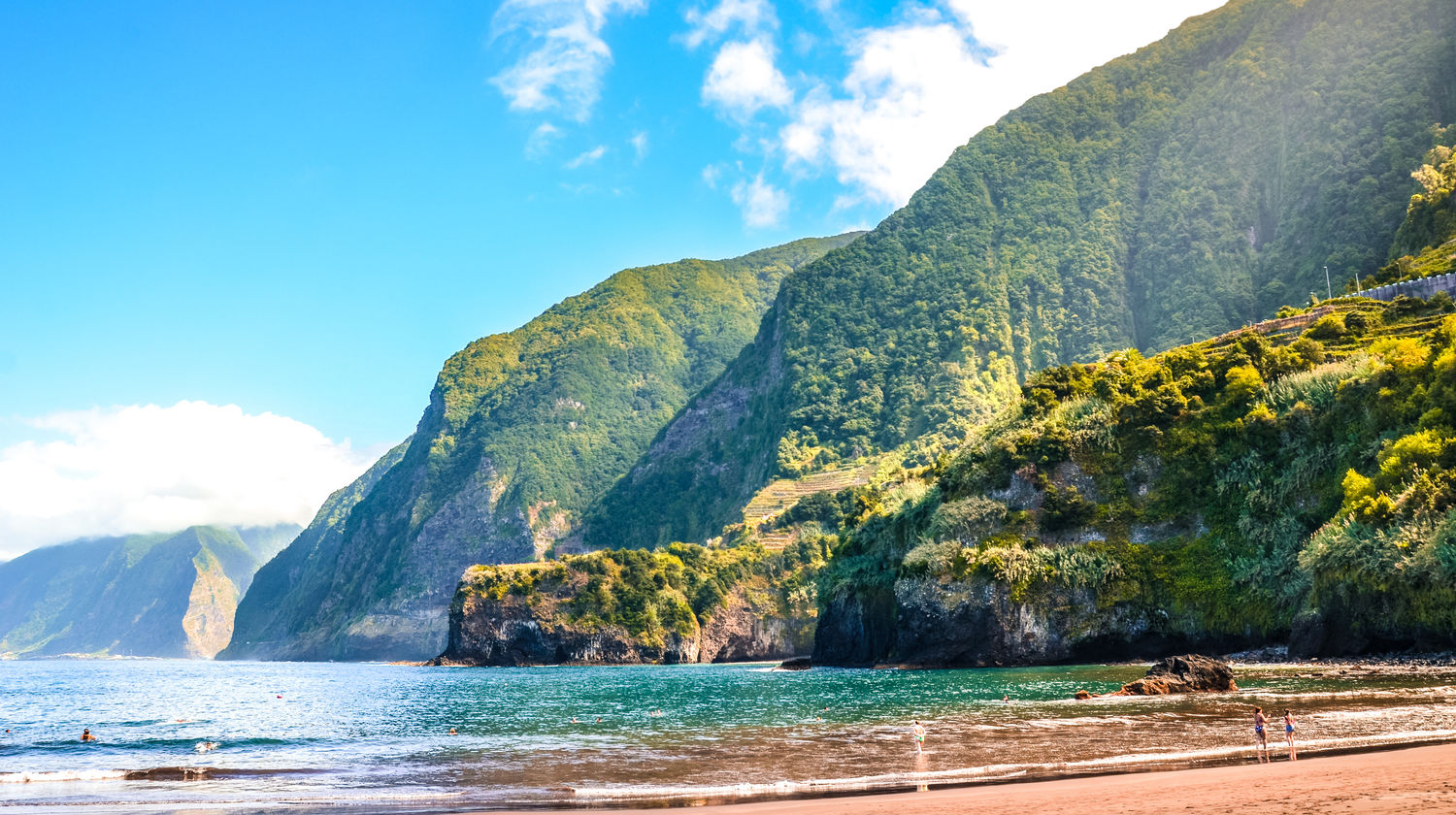 Dramatic coastal cliffs and black sand beach at Seixal, with lush green slopes and turquoise Atlantic waters on Madeira’s north coast