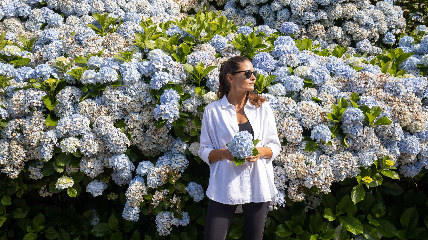Woman standing next to vibrant blue hydrangeas on a country path in São Miguel Island, Azores