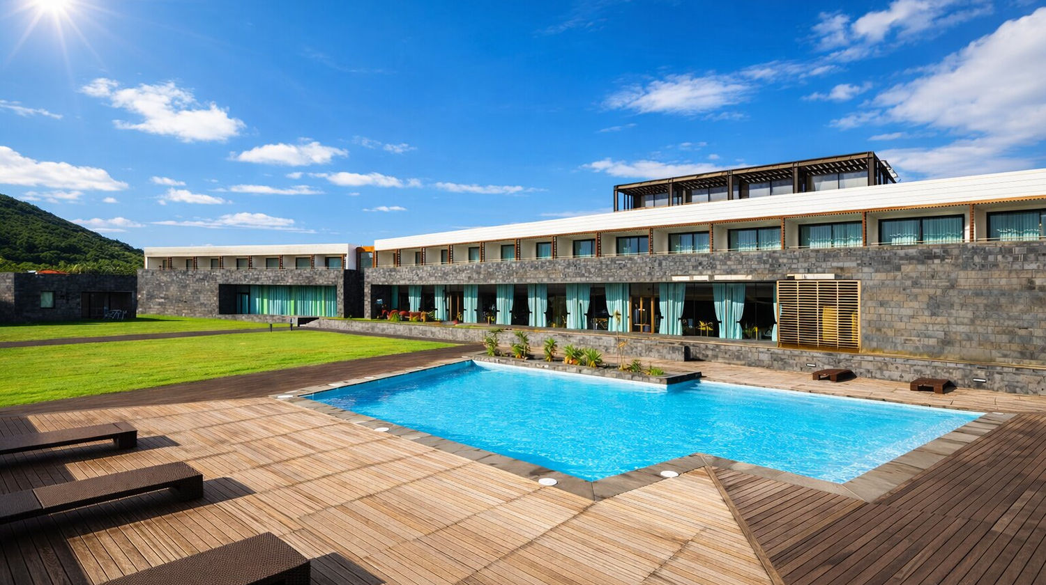 Piscina exterior do Hotel da Graciosa 4 estrelas com edifício moderno em pedra e espreguiçadeiras sob céu azul na Ilha Graciosa.
