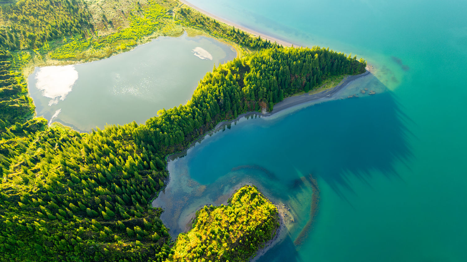 Vista aérea da Lagoa do Fogo, na Ilha de São Miguel, mostrando a lagoa de origem vulcânica rodeada por encostas cobertas de vegetação nativa.