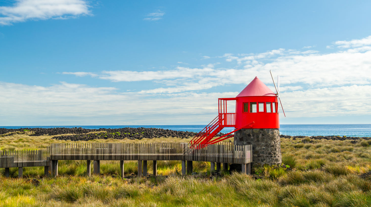 Moinho vermelho no Moinho do Juncal rodeado por campos verdes com vista para o oceano na Ilha do Pico, Açores