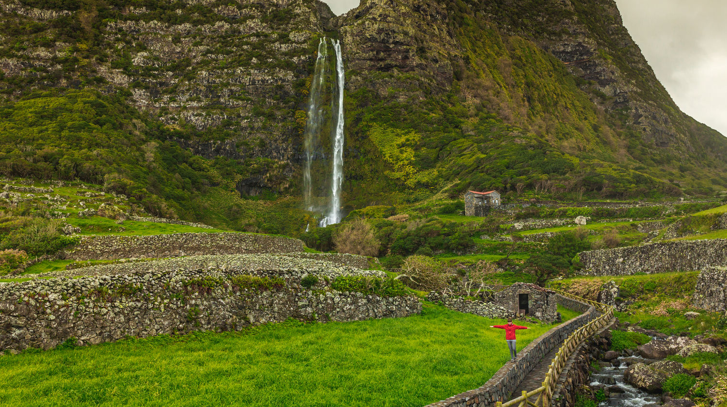 Cascata do Poço do Bacalhau a cair por falésias cobertas de vegetação verde exuberante, Ilha das Flores, Açores