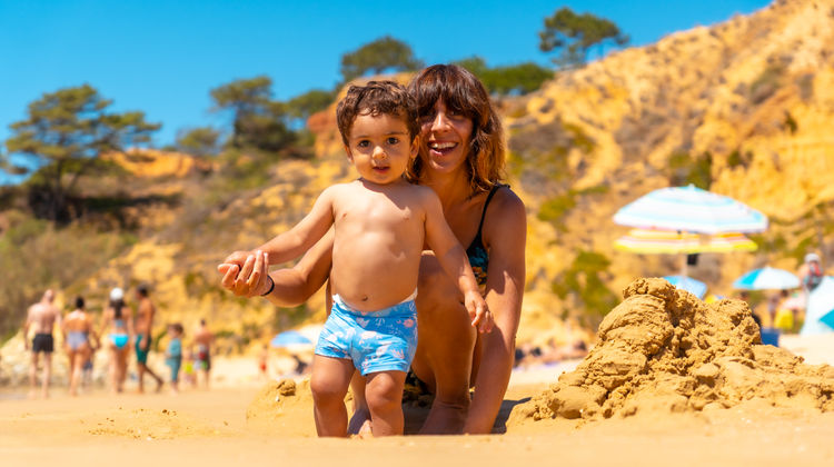 Mother and child enjoying quality time together on the beach in Algarve, surrounded by stunning golden rocks.