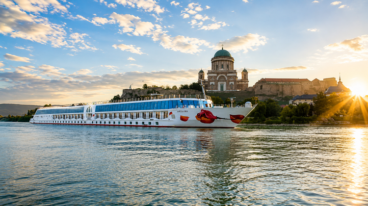 A river cruise ship sailing on the Danube River in Budapest, Hungary, with the city's historic skyline and riverside architecture visible along the waterfront.