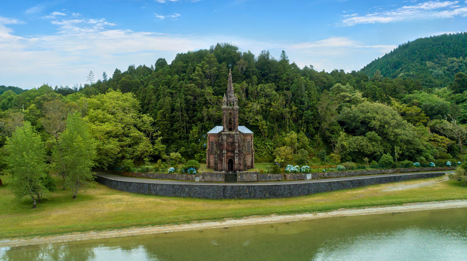 Nossa Senhora das Vitórias Chapel reflected in Lagoa das Furnas, surrounded by lush greenery in Furnas, São Miguel Island, Azores