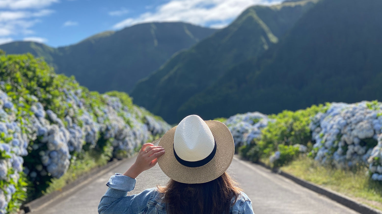 Person walking along a mountain road surrounded by green hills and hydrangeas in Sete Cidades, São Miguel Island, Azores