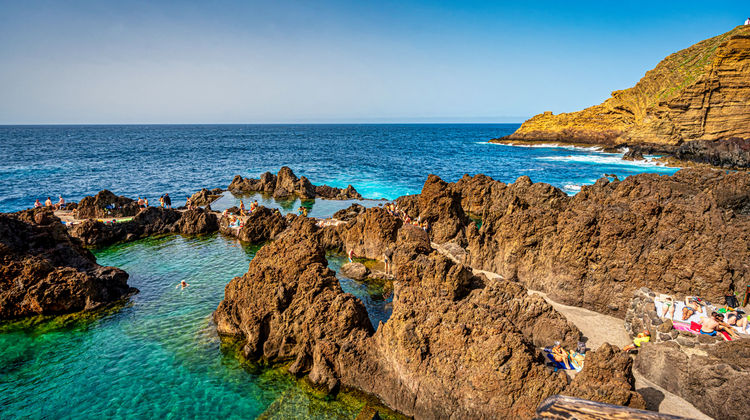 Volcanic natural pools in Porto Moniz, Madeira, Portugal, formed by lava rock along the Atlantic coastline. The pools are filled with seawater and surrounded by rugged volcanic formations.