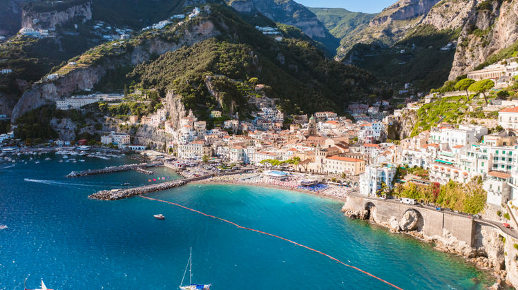 Aerial view of Amalfi on Italy's Amalfi Coast, showing colorful buildings clustered between the mountains and the Mediterranean Sea. Amalfi is a popular day trip destination from Salerno Cruise Port.
