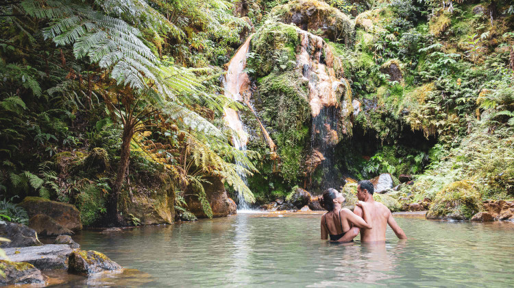 People relaxing in a warm geothermal spring at Caldeira Velha surrounded by lush forest on São Miguel Island