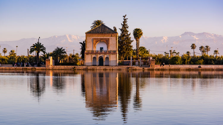 Scenic view of the Menara Gardens in Marrakesh, featuring a tranquil olive grove and a reflecting pool with the Atlas Mountains in the background, offering a peaceful escape in the heart of the city