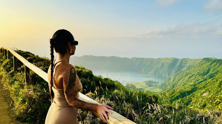Woman gazing at lush green volcanic crater at Miradouro da Boca do Inferno on São Miguel Island.