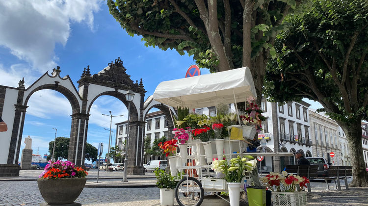 Portas da Cidade city gates with white arches and a flower stand in the foreground in Ponta Delgada, São Miguel Island, Azores