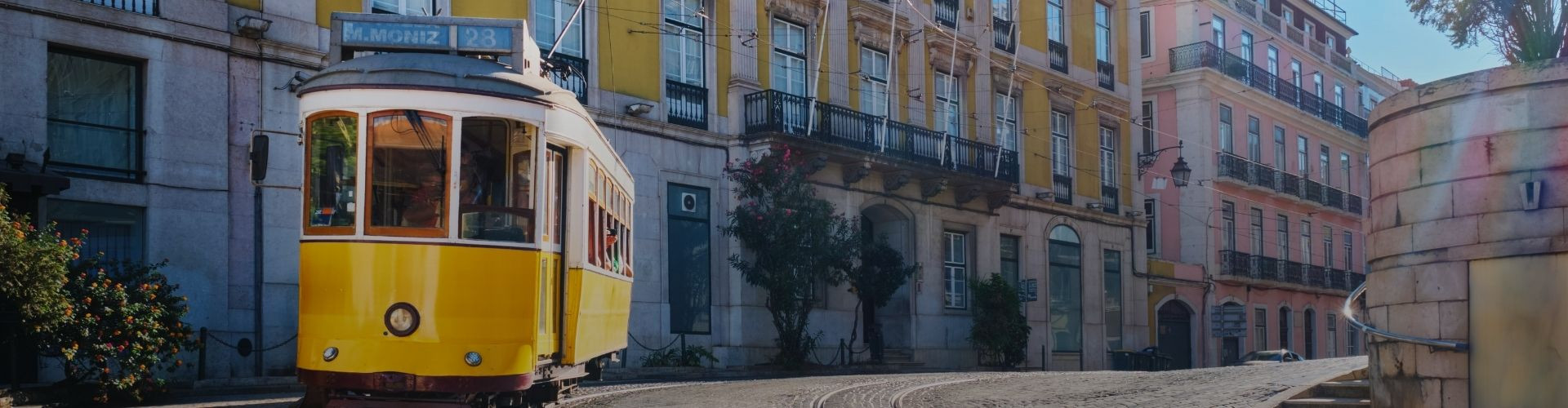 Lisbon’s iconic yellow Tram 28 travels along a cobbled street lined with colorful historic buildings in the city center.