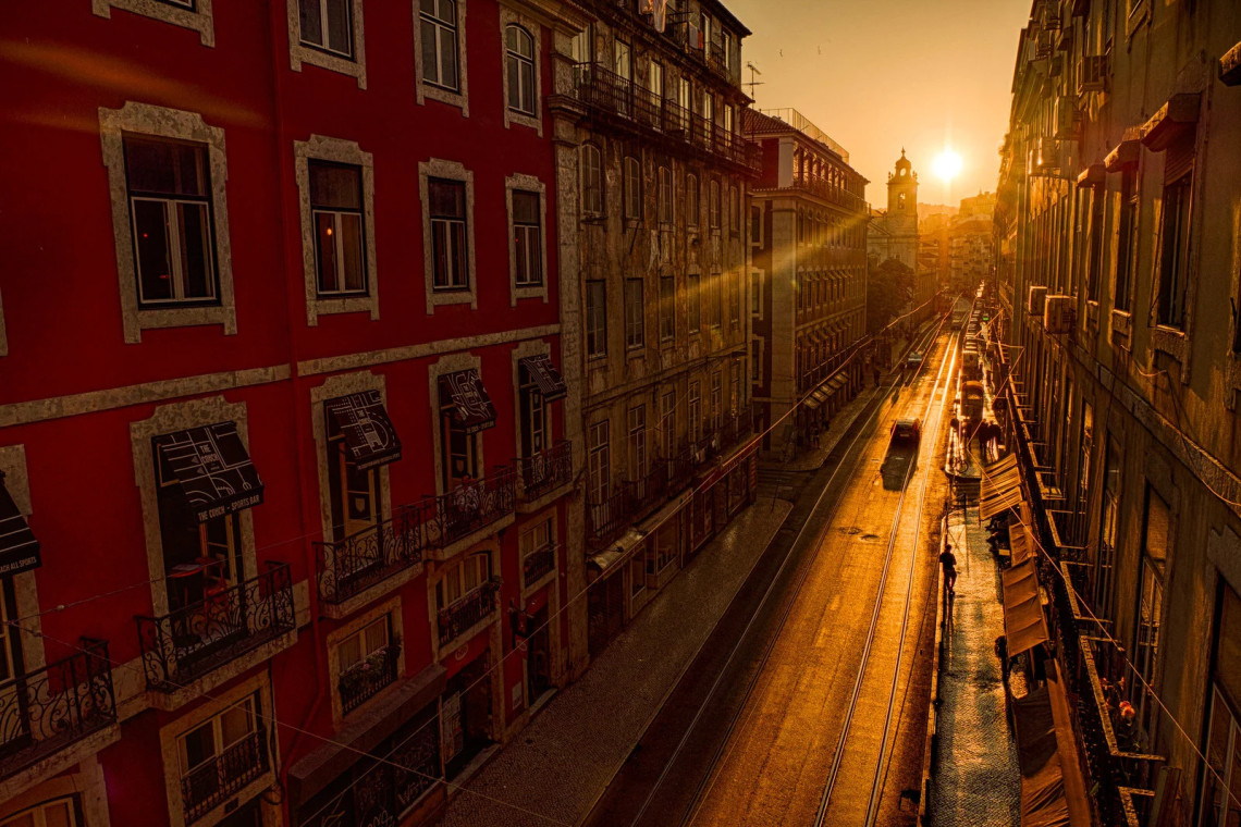 Aerial view of a narrow tram street in Baixa Chiado neighbourhood at sunset in Lisbon, Portugal, with golden sunlight flooding between historic buildings