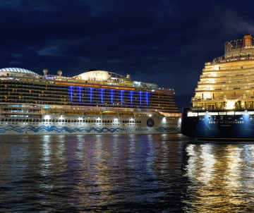 Large cruise ships illuminated at night while docked at Lisbon Cruise Port, Portugal, with their lights reflected across the dark waters of the Tagus River.