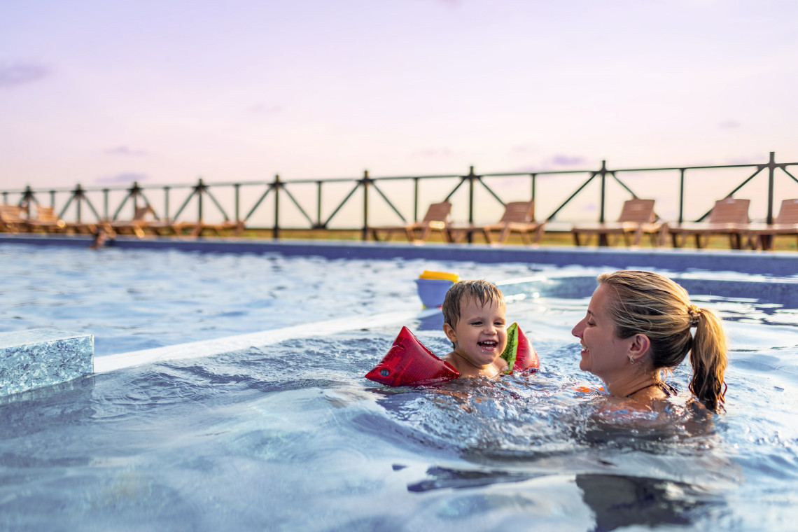 Mother and child playing in a swimming pool at a family-friendly all-inclusive resort in the Algarve, Portugal, during a sunny afternoon.