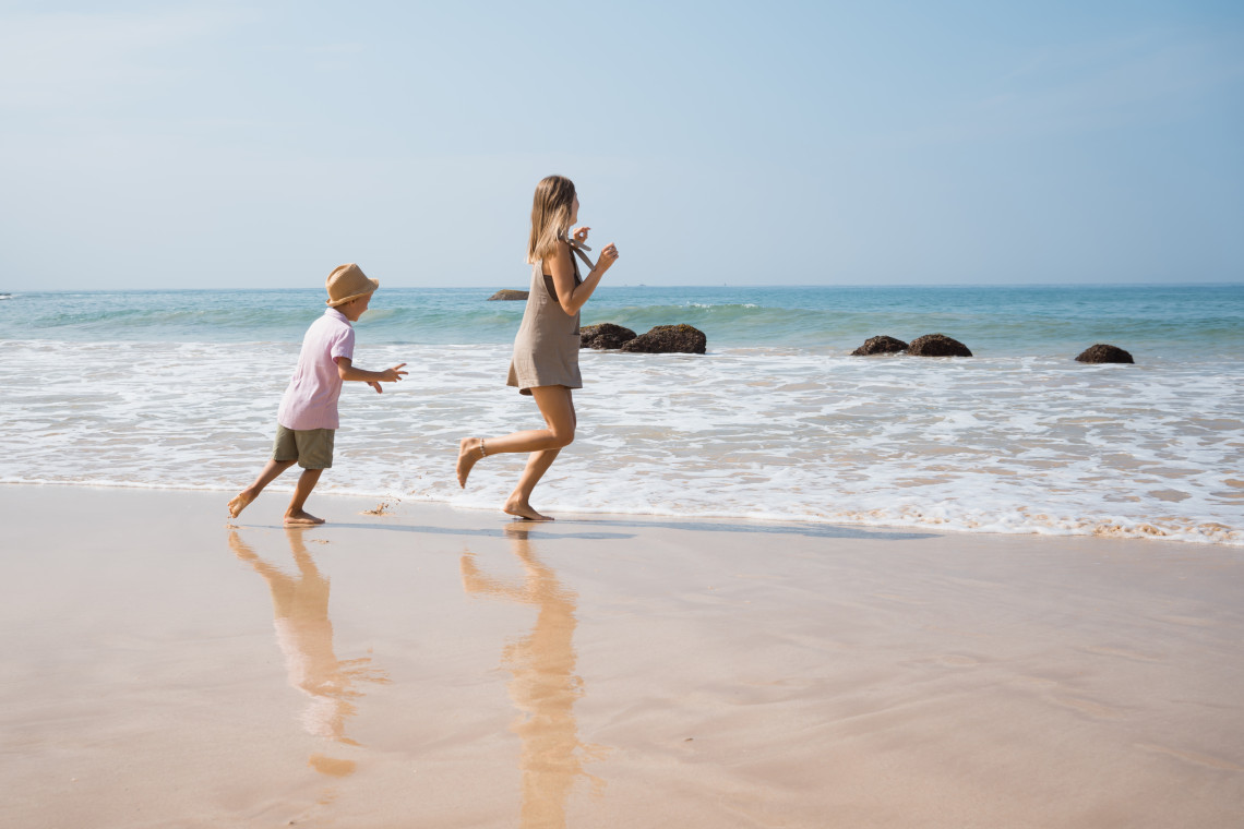 A mother and child playing by the shoreline on a sunny Algarve beach in Portugal, enjoying a relaxed family vacation at an all-inclusive resort.