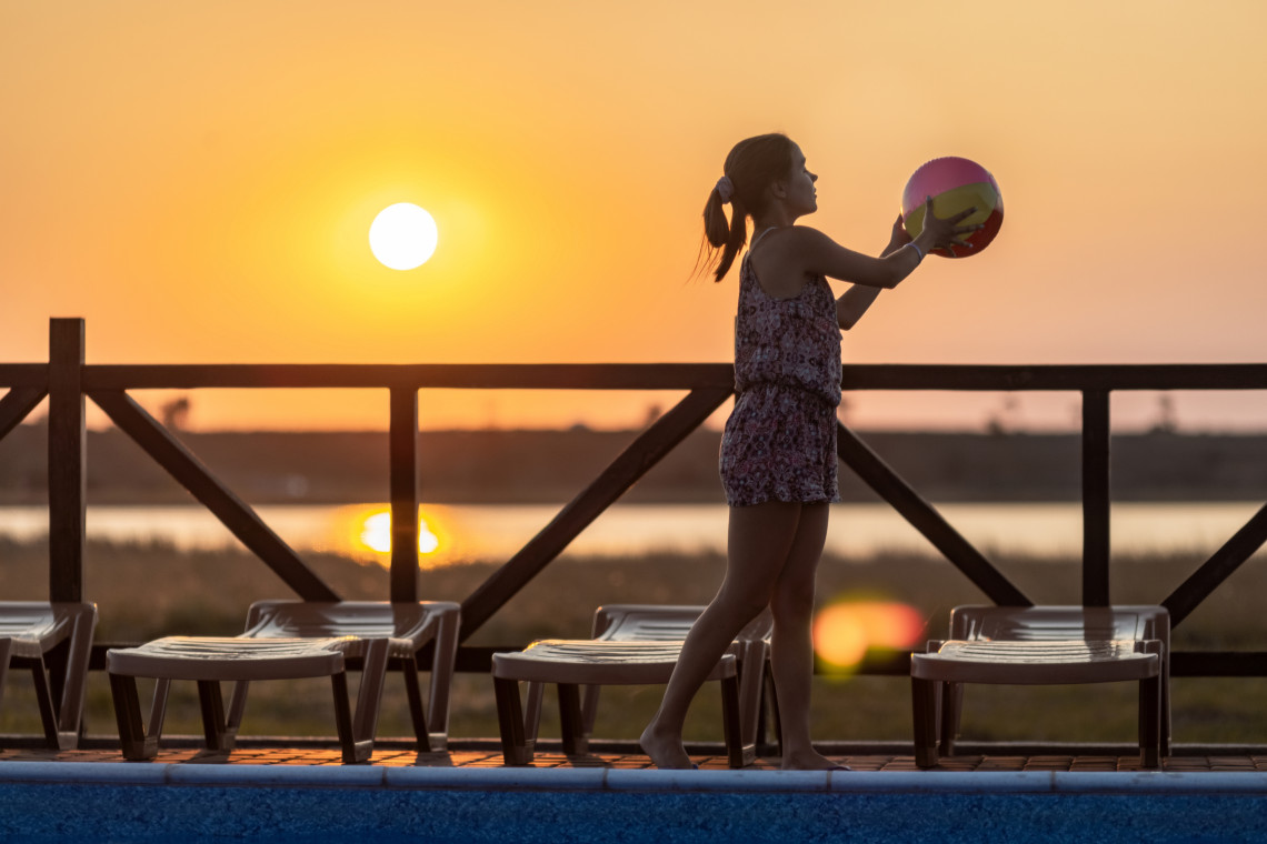 Child playing with a beach ball by the pool at sunset in a family-friendly all-inclusive resort in the Algarve, Portugal.
