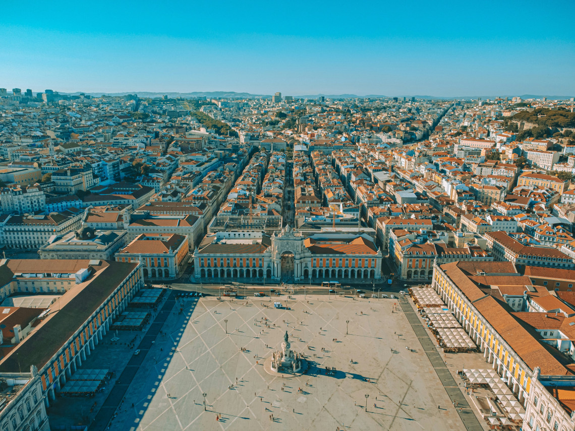 Aerial view of Pra&ccedil;a do Com&eacute;rcio and the Baixa district in central Lisbon, Portugal. The open riverside square, equestrian statue and symmetrical arcaded buildings lead toward the city&rsquo;s terracotta rooftops and historic streets.