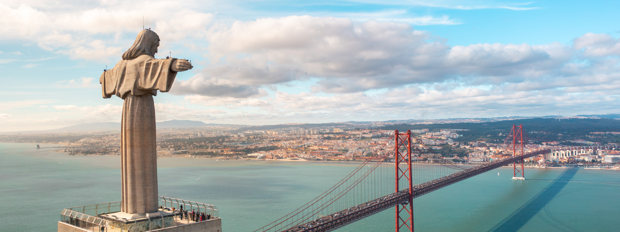 Panoramic view of the Cristo Rei monument in Almada overlooking the 25 de Abril Bridge, Tagus River and the city of Lisbon beyond.