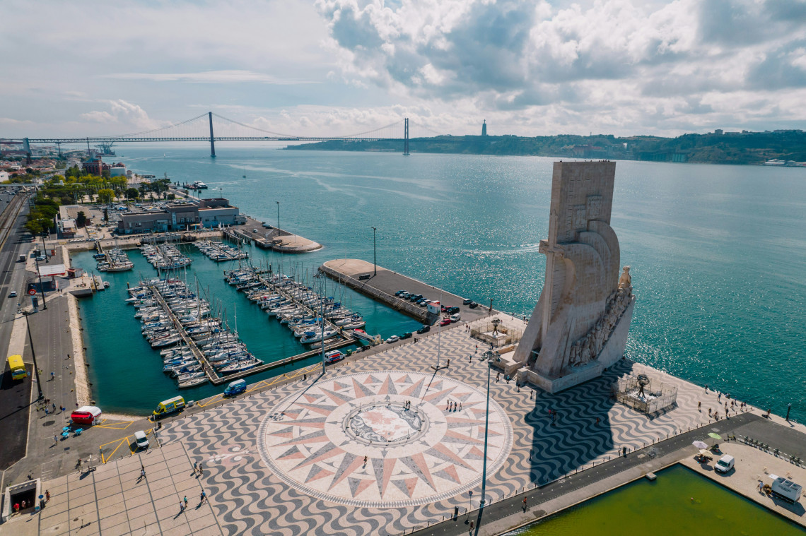 Aerial view of the Monument to the Discoveries and its iconic wind rose mosaic pavement on the Bel&eacute;m waterfront, with the marina and 25 de Abril Bridge along the Tagus River in Lisbon, Portugal