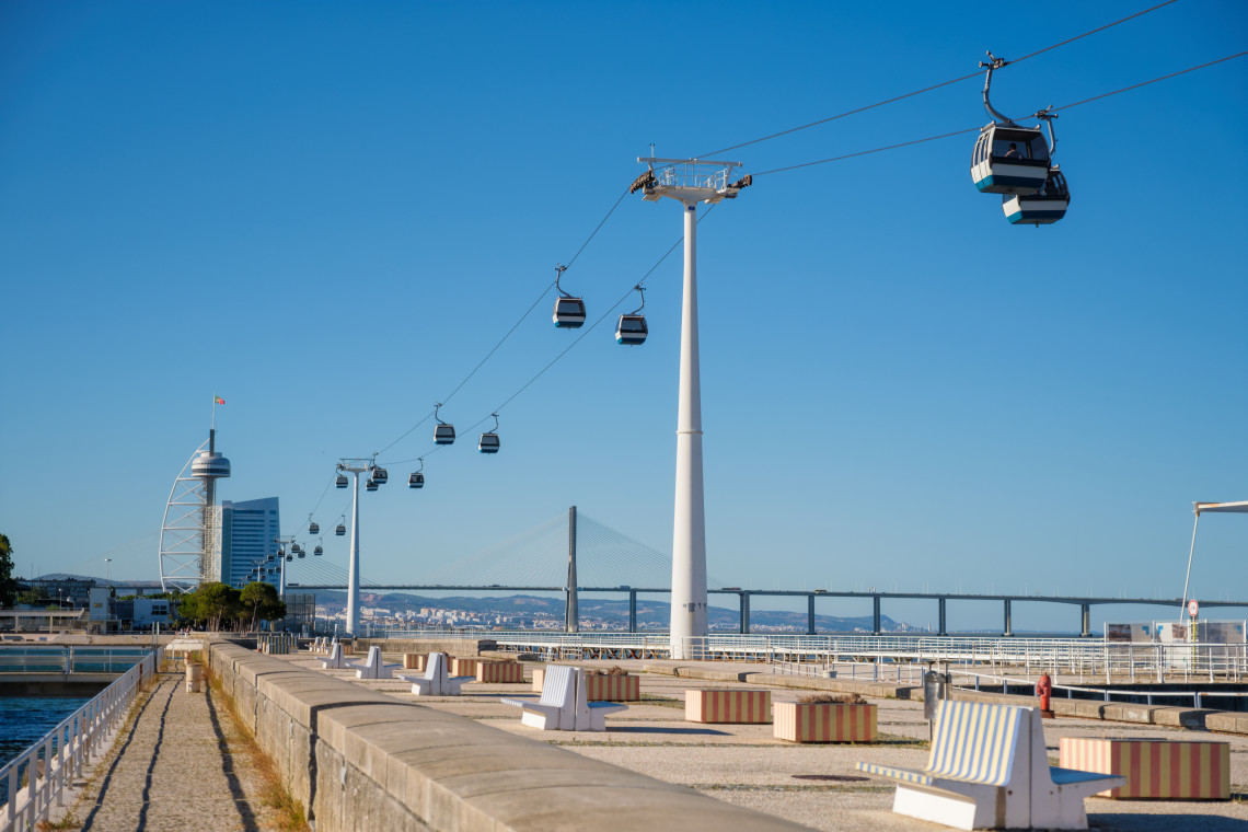 Cable car gondolas over the Parque das Na&ccedil;&otilde;es waterfront in Lisbon with the Vasco da Gama Tower and Vasco da Gama Bridge in the background on a clear sunny day