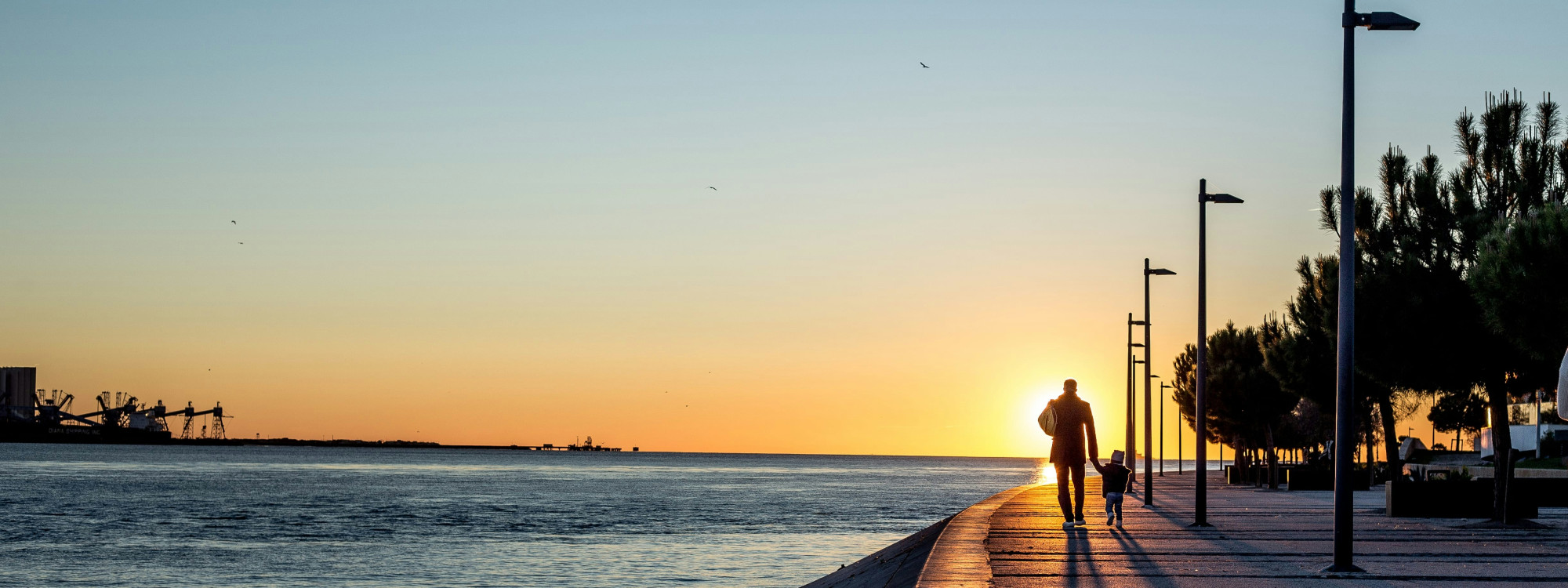 Person walking along the Tagus riverside promenade at sunset in Lisbon, Portugal