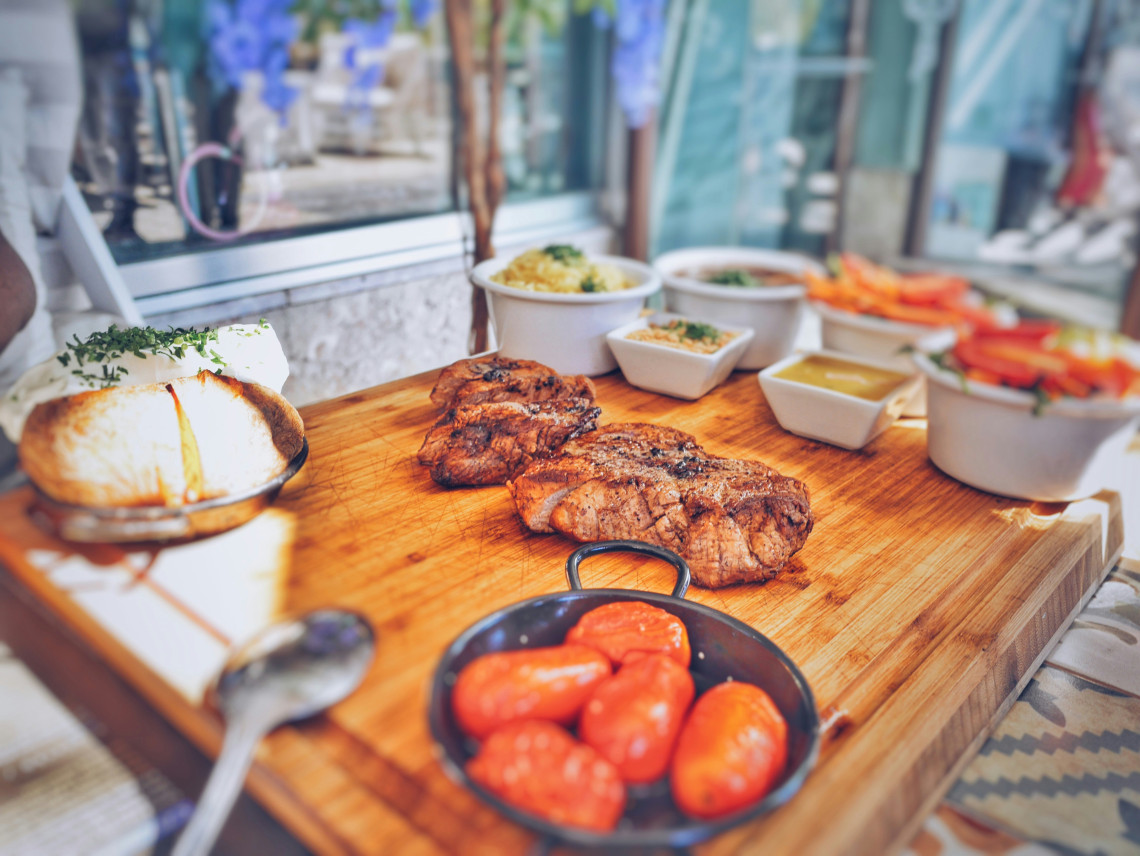 Traditional Portuguese meat dish served on a wooden board with roasted tomatoes, fresh cheese, rice and side sauces at a restaurant in Lisbon