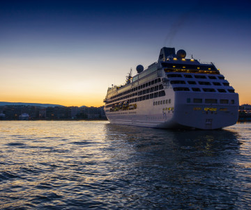 Large cruise ship sailing beside the port of Funchal on Madeira Island, Portugal, as the evening sky fades into sunset over the Atlantic Ocean.