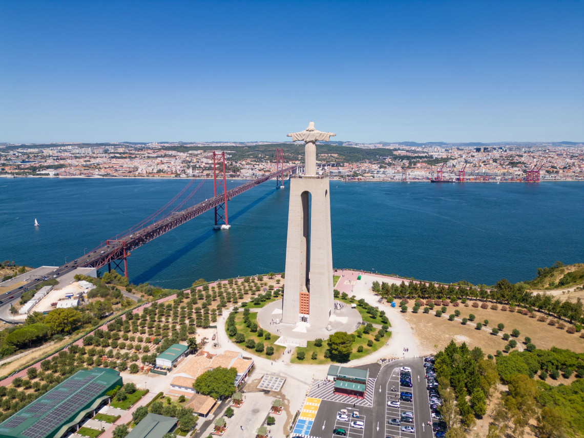 Aerial view of Christ the King statue in Almada with the 25 de Abril Bridge and Lisbon skyline across the Tagus River on a clear sunny day