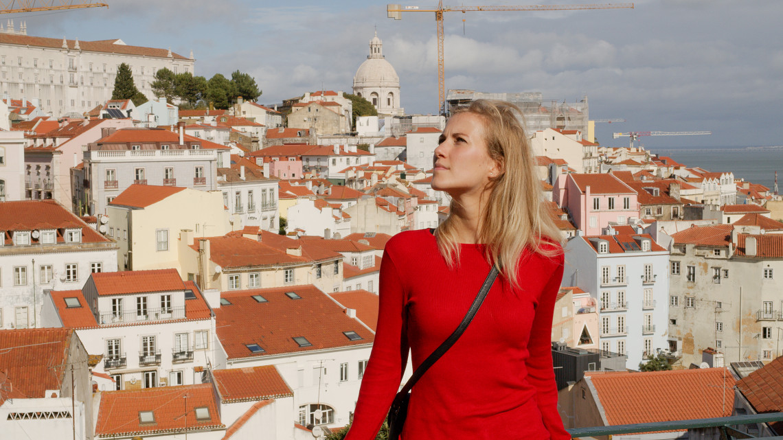 Woman in a red dress enjoying the panoramic view over Alfama's terracotta rooftops and the National Pantheon dome from a miradouro in Lisbon, Portugal