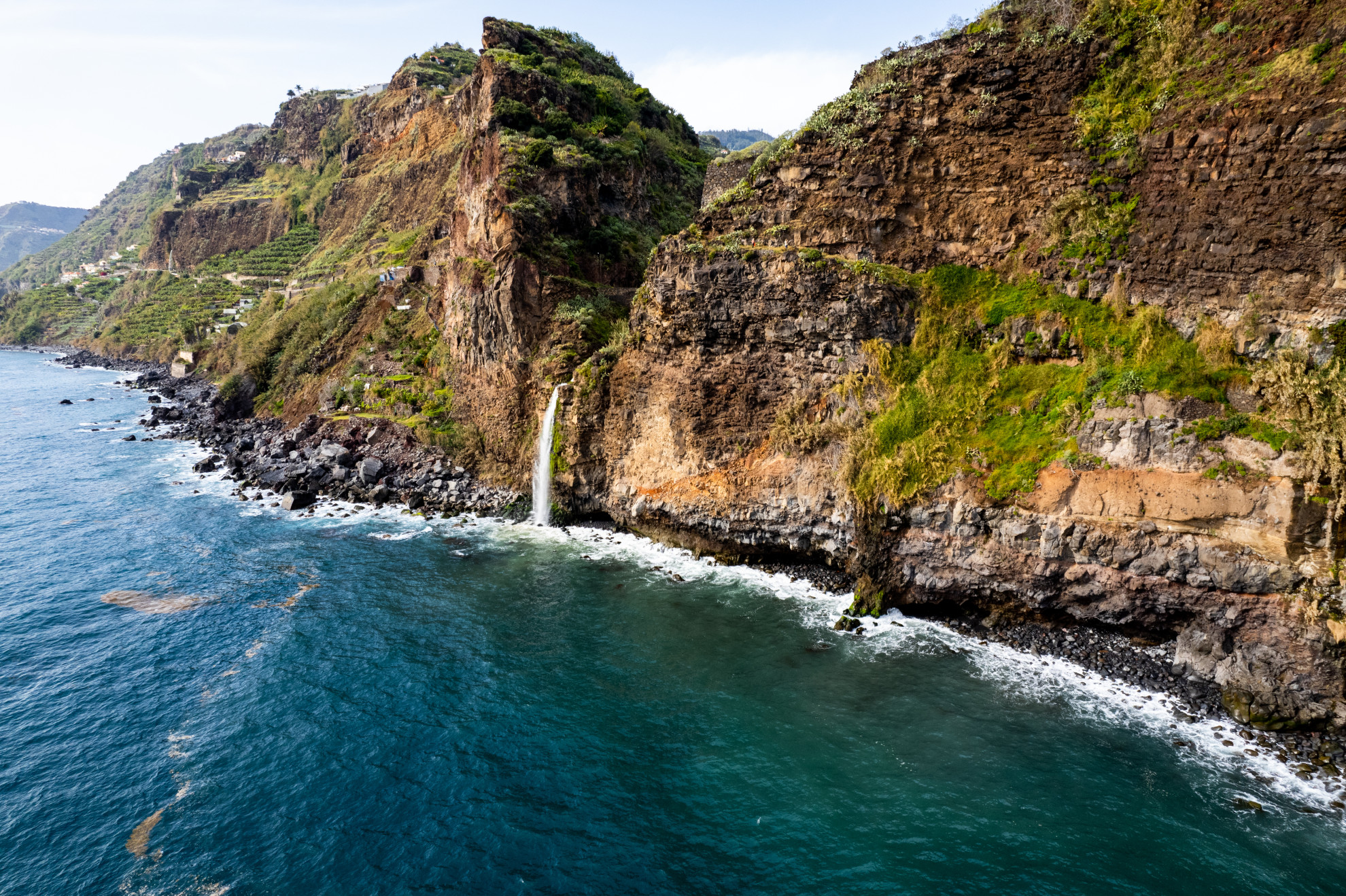 Rugged volcanic coastline near Ponta do Sol, Madeira, with dramatic green cliffs, rocky shores and turquoise Atlantic water