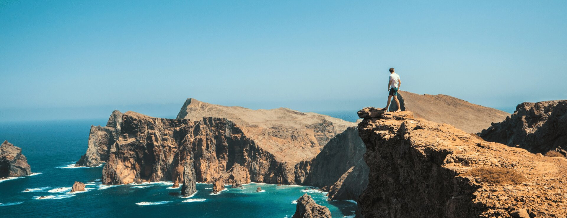A person standing on a dramatic clifftop viewpoint on Madeira, looking out over the Atlantic Ocean with rugged volcanic coastline below