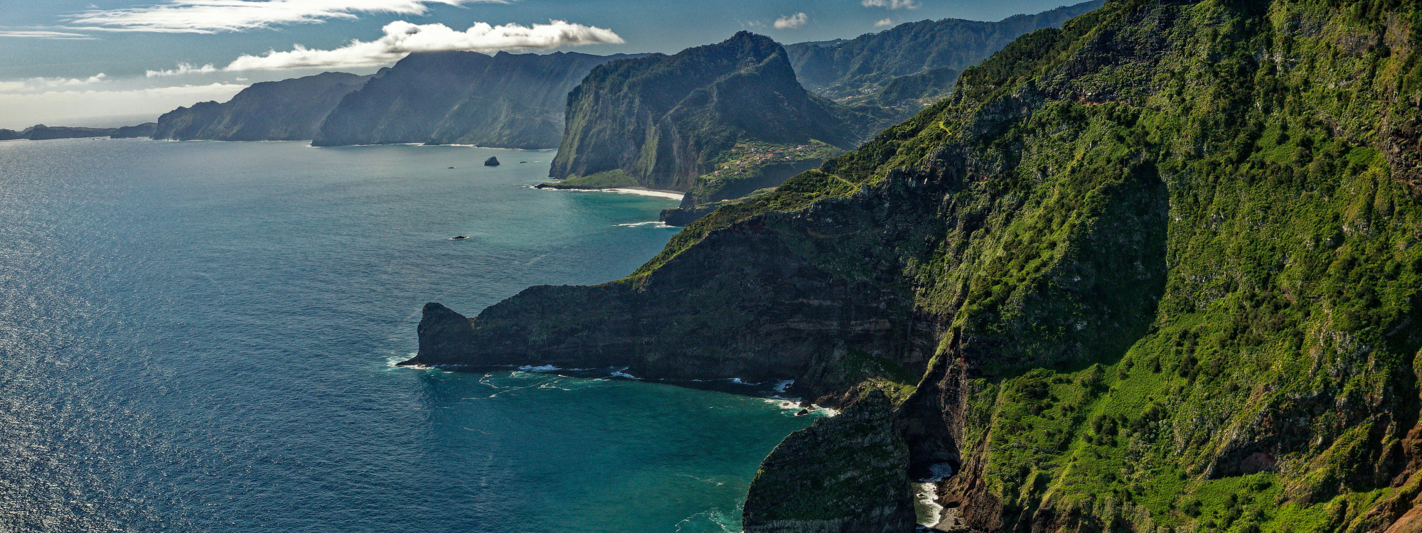 Aerial view of steep green cliffs along Madeira's coastline, a scenic backdrop for island vacations