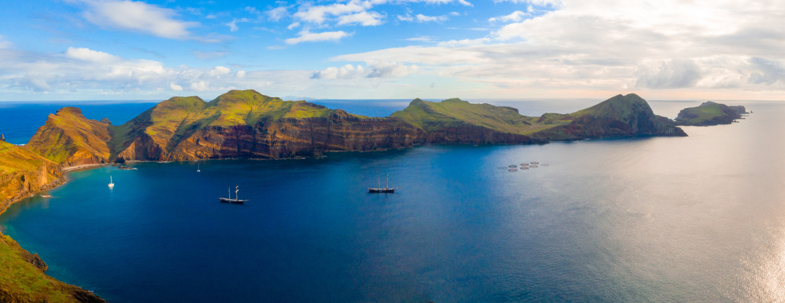Ponta de S&atilde;o Louren&ccedil;o in Cani&ccedil;al, Madeira Island, Portugal, with rugged volcanic cliffs, blue Atlantic water, and boats anchored near the coastline. The image shows the island&rsquo;s eastern peninsula and its distinctive coastal landscape.