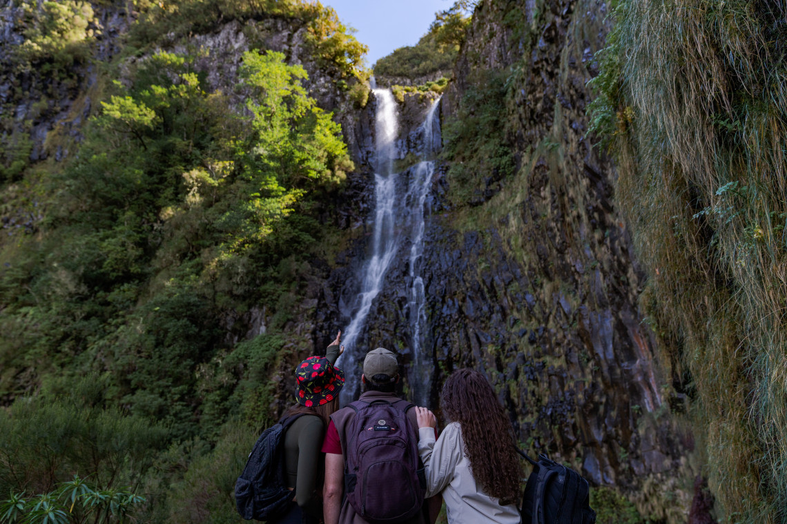 Hikers stand facing the waterfall at Levada do Risco in Calheta, Madeira Island, Portugal. The image shows one of Madeira&rsquo;s best-known levada walks, surrounded by steep rock walls and dense green vegetation in the Raba&ccedil;al area.