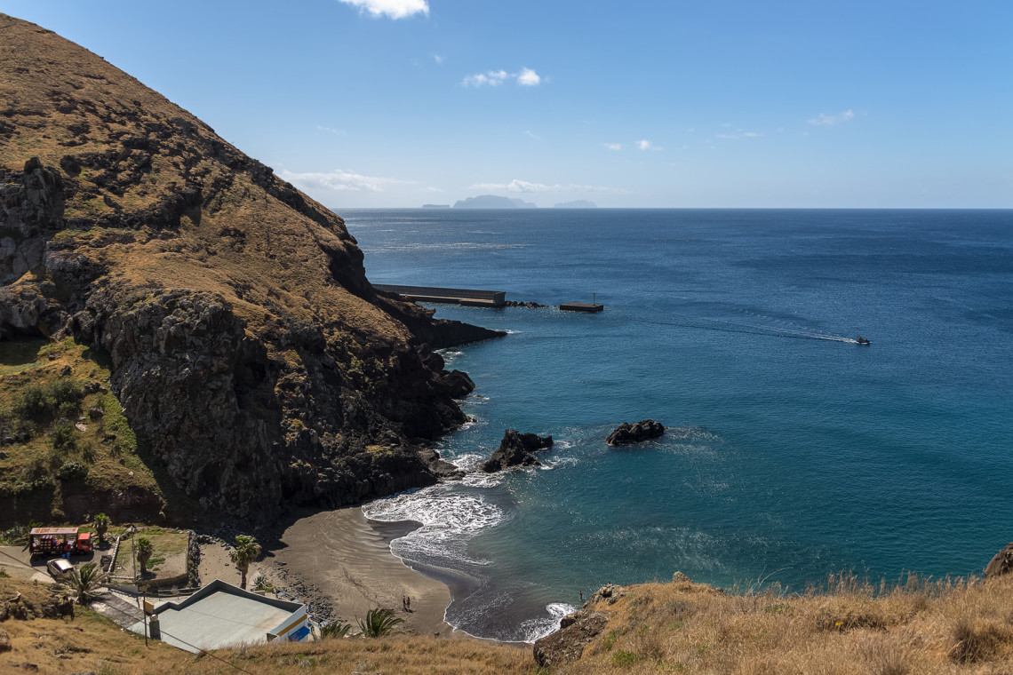 Elevated view of Prainha Beach near Cani&ccedil;al, Madeira, Portugal, showing a small dark sand cove surrounded by dry volcanic cliffs. The sheltered beach opens onto the blue Atlantic Ocean near Madeira&rsquo;s eastern tip.